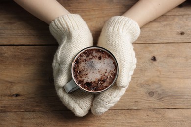 Photo of Woman holding mug of tasty hot chocolate at wooden table, top view