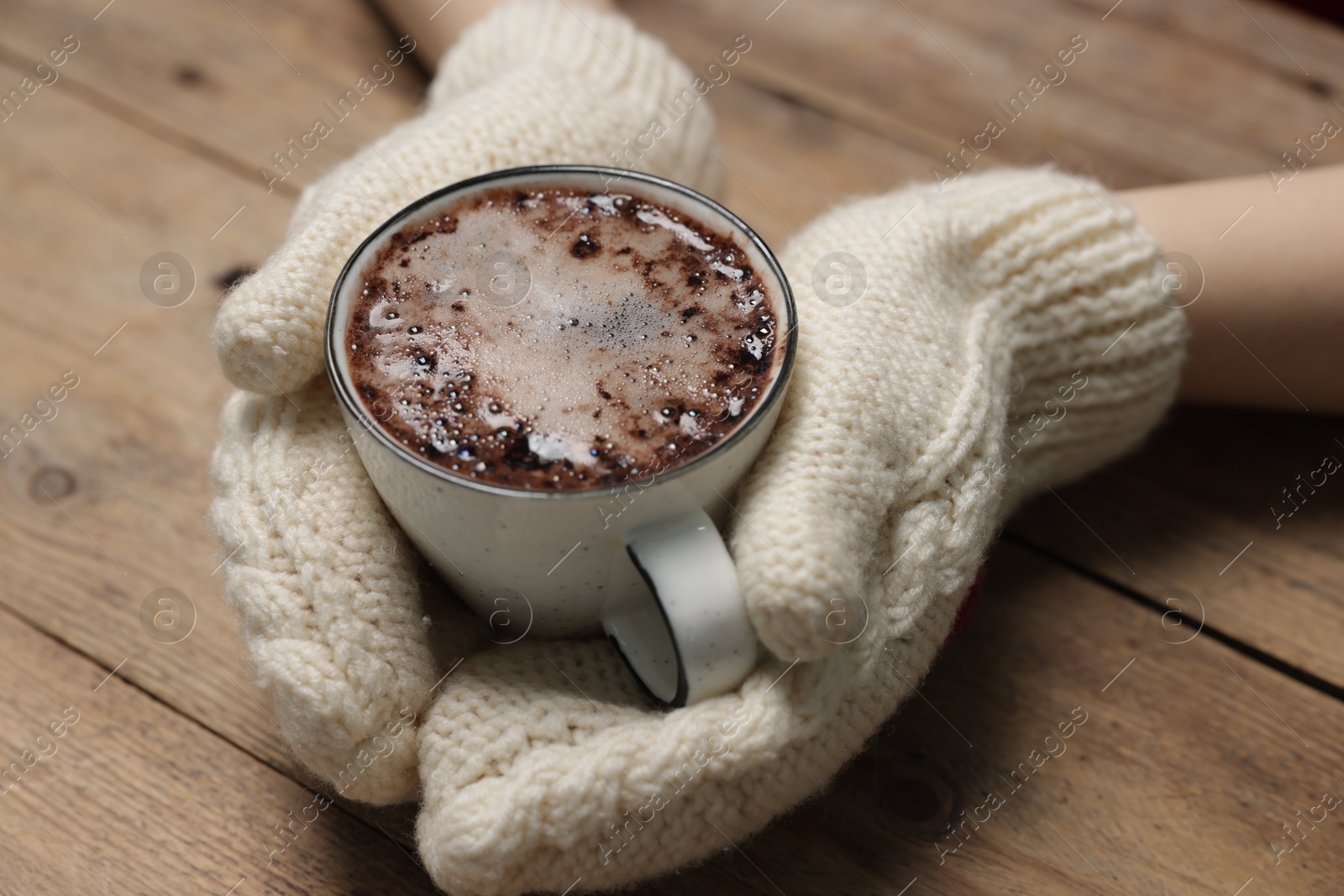 Photo of Woman holding mug of tasty hot chocolate at wooden table, closeup