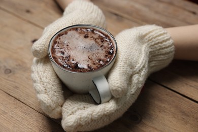 Photo of Woman holding mug of tasty hot chocolate at wooden table, closeup