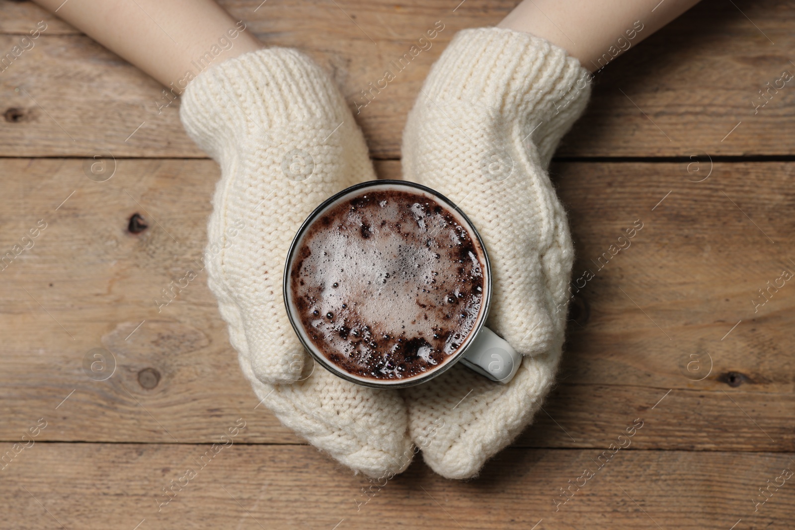 Photo of Woman holding mug of tasty hot chocolate at wooden table, top view