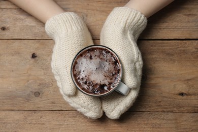 Photo of Woman holding mug of tasty hot chocolate at wooden table, top view