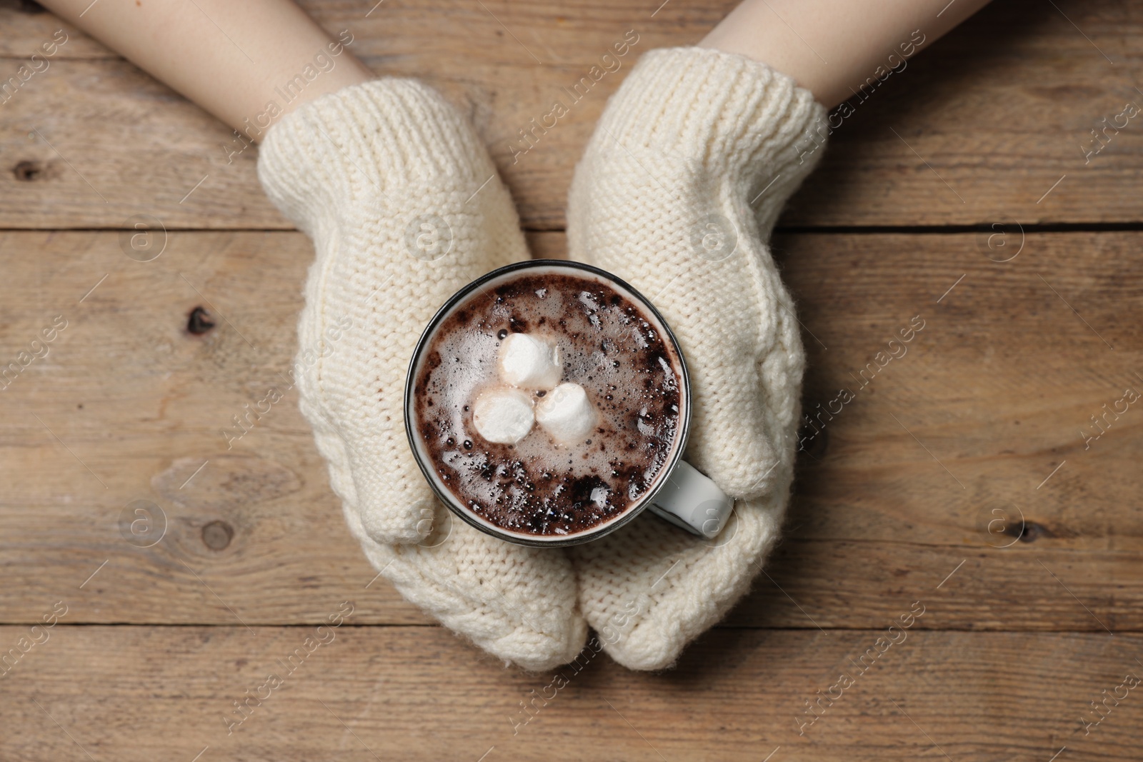 Photo of Woman holding mug of tasty hot chocolate with marshmallows at wooden table, top view