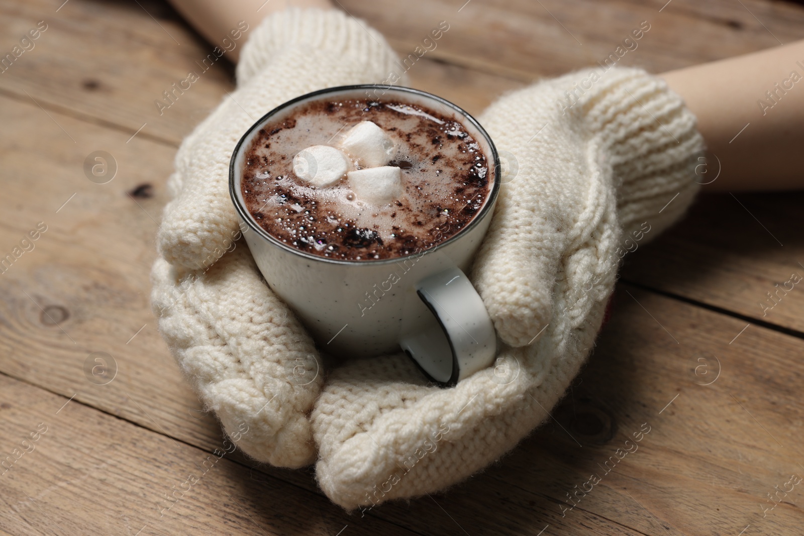 Photo of Woman holding mug of tasty hot chocolate with marshmallows at wooden table, closeup