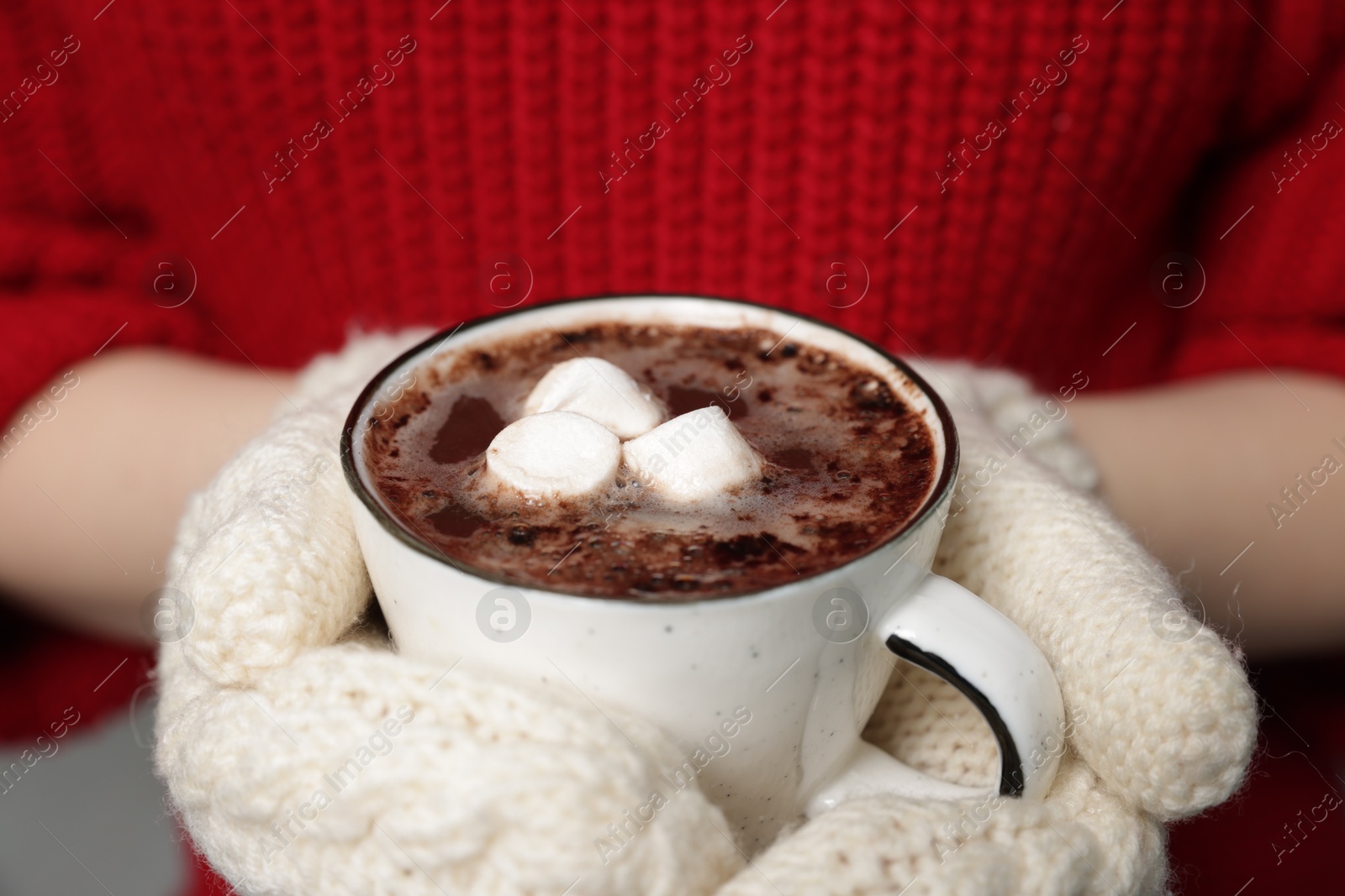 Photo of Woman holding mug of tasty hot chocolate with marshmallows indoors, closeup