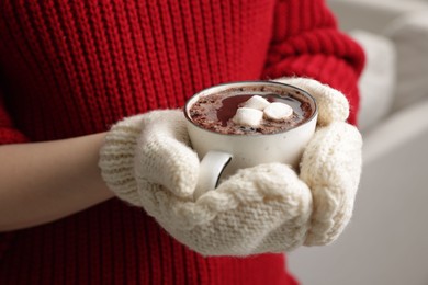 Photo of Woman holding mug of tasty hot chocolate with marshmallows indoors, closeup