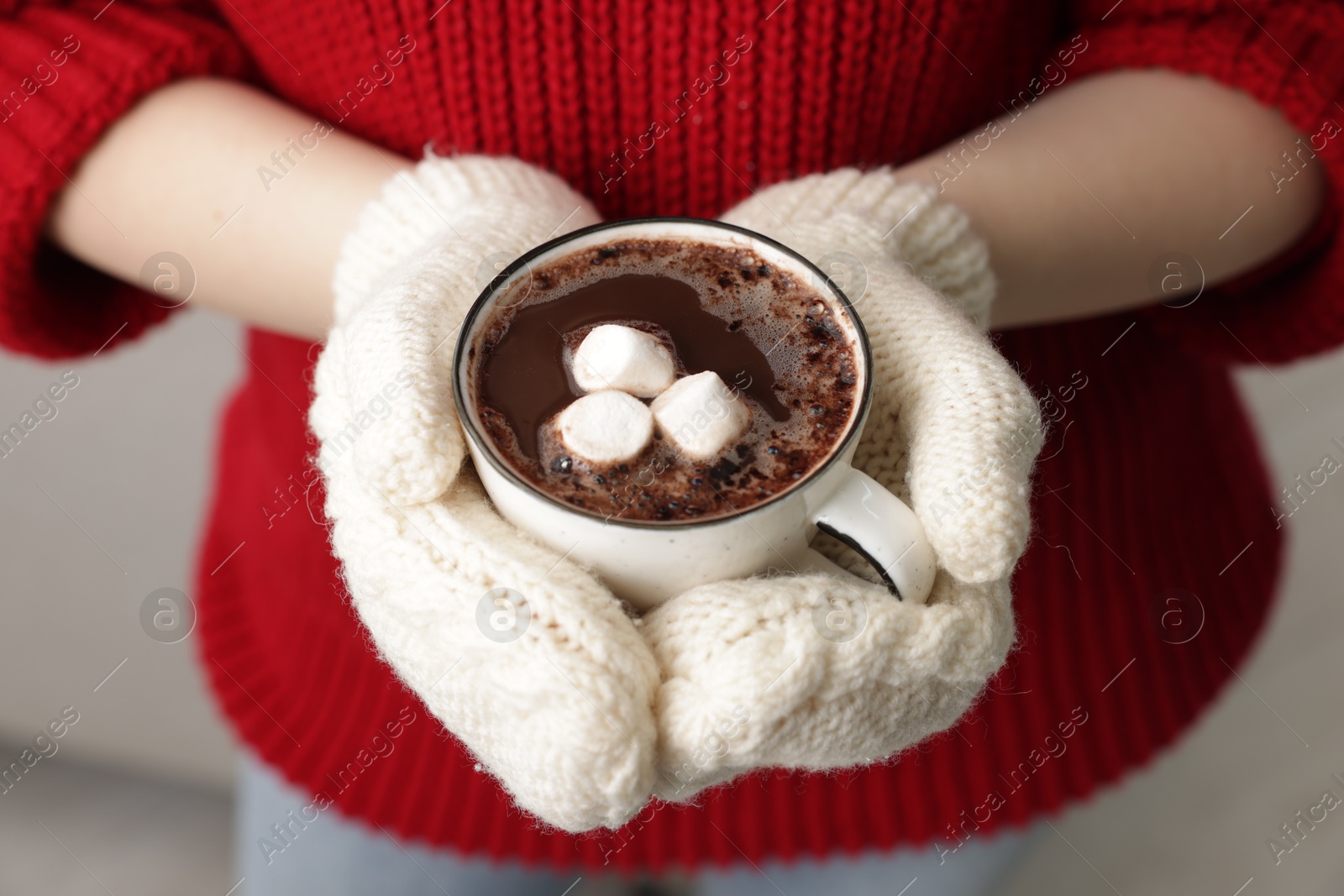 Photo of Woman holding mug of tasty hot chocolate with marshmallows indoors, closeup