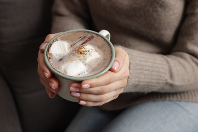 Photo of Woman holding mug of tasty hot chocolate with marshmallows and cinnamon indoors, closeup