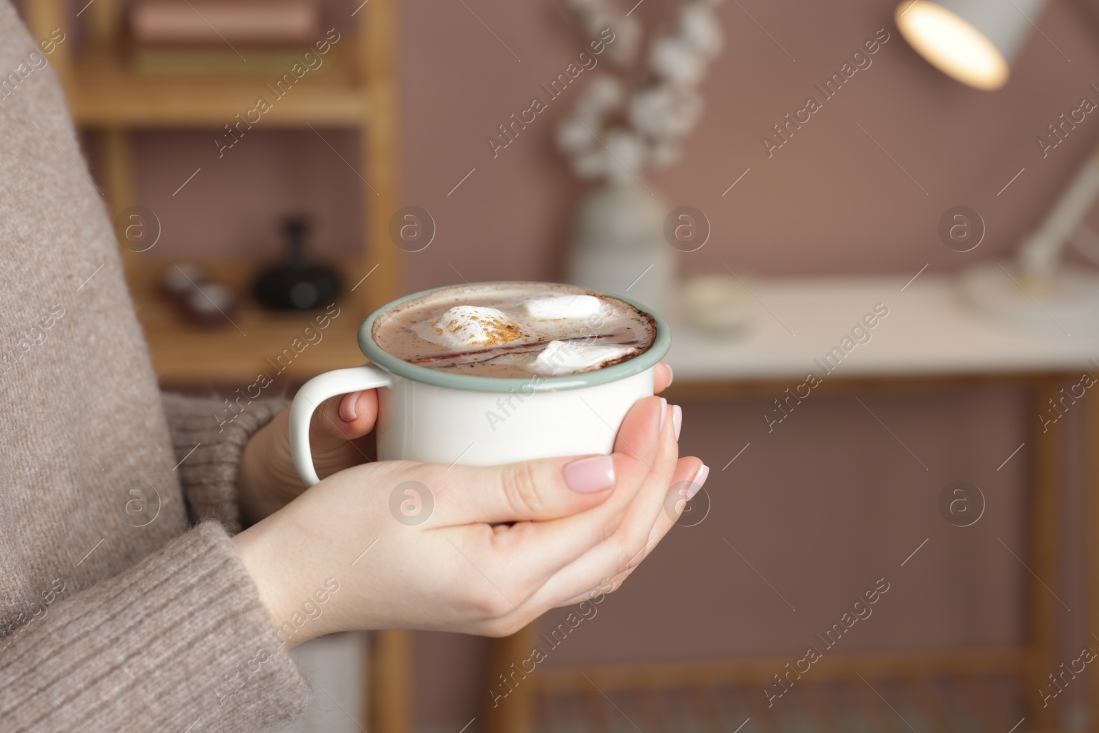 Photo of Woman holding mug of tasty hot chocolate with marshmallows and cinnamon indoors, closeup. Space for text