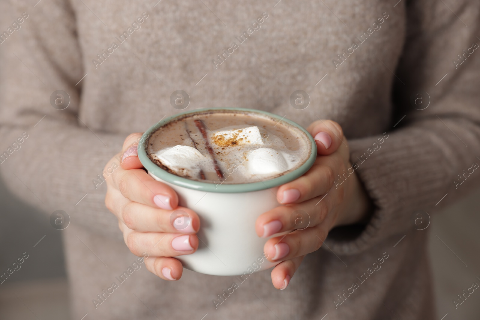 Photo of Woman holding mug of tasty hot chocolate with marshmallows and cinnamon indoors, closeup