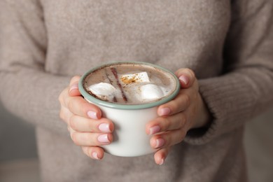 Photo of Woman holding mug of tasty hot chocolate with marshmallows and cinnamon indoors, closeup