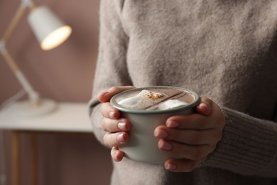 Photo of Woman holding mug of tasty hot chocolate with marshmallows and cinnamon indoors, closeup