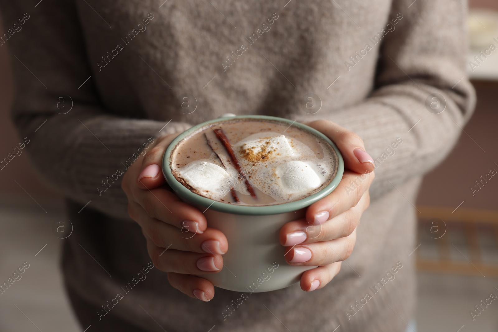 Photo of Woman holding mug of tasty hot chocolate with marshmallows and cinnamon indoors, closeup