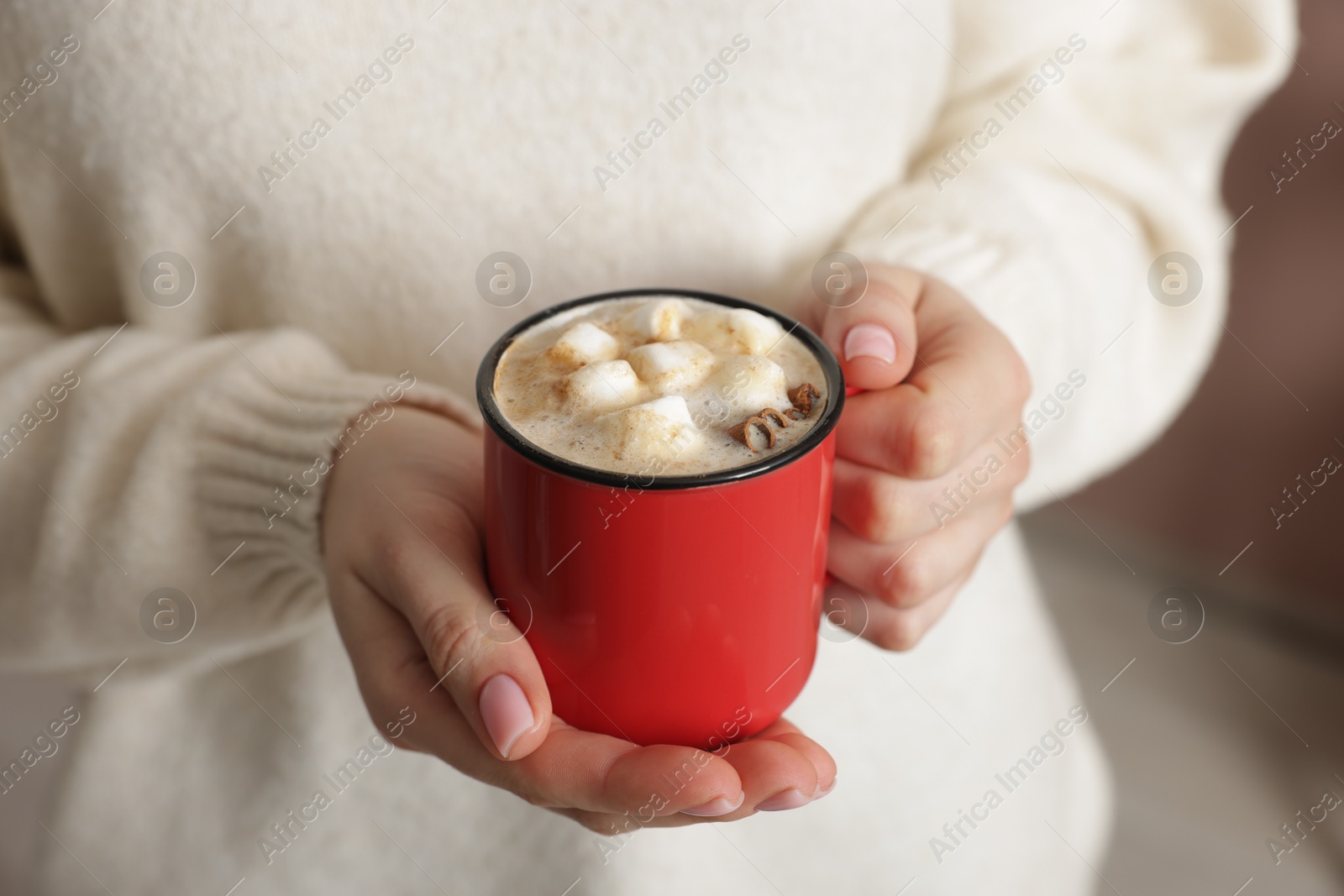 Photo of Woman holding mug of tasty hot chocolate with marshmallows and cinnamon indoors, closeup