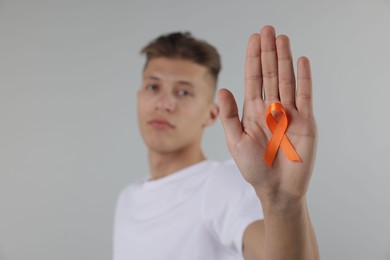 Photo of Multiple Sclerosis awareness. Man with orange ribbon on light grey background, selective focus