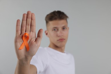 Photo of Multiple Sclerosis awareness. Man with orange ribbon on light grey background, selective focus