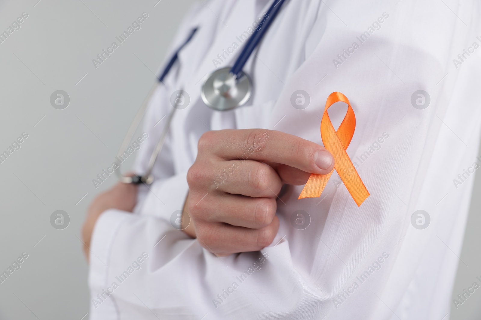 Photo of Multiple Sclerosis awareness. Doctor with orange ribbon on light grey background, closeup