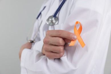 Photo of Multiple Sclerosis awareness. Doctor with orange ribbon on light grey background, closeup