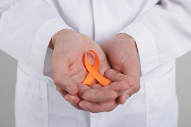 Photo of Multiple Sclerosis awareness. Doctor with orange ribbon on light grey background, closeup