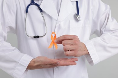 Photo of Multiple Sclerosis awareness. Doctor with orange ribbon on light grey background, closeup