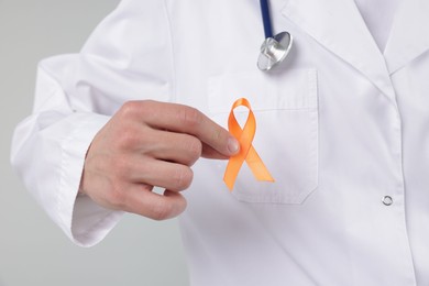 Photo of Multiple Sclerosis awareness. Doctor with orange ribbon on light grey background, closeup