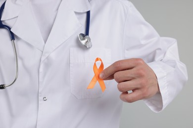 Photo of Multiple Sclerosis awareness. Doctor with orange ribbon on light grey background, closeup