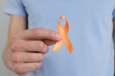 Photo of Multiple Sclerosis awareness. Man with orange ribbon on light grey background, closeup