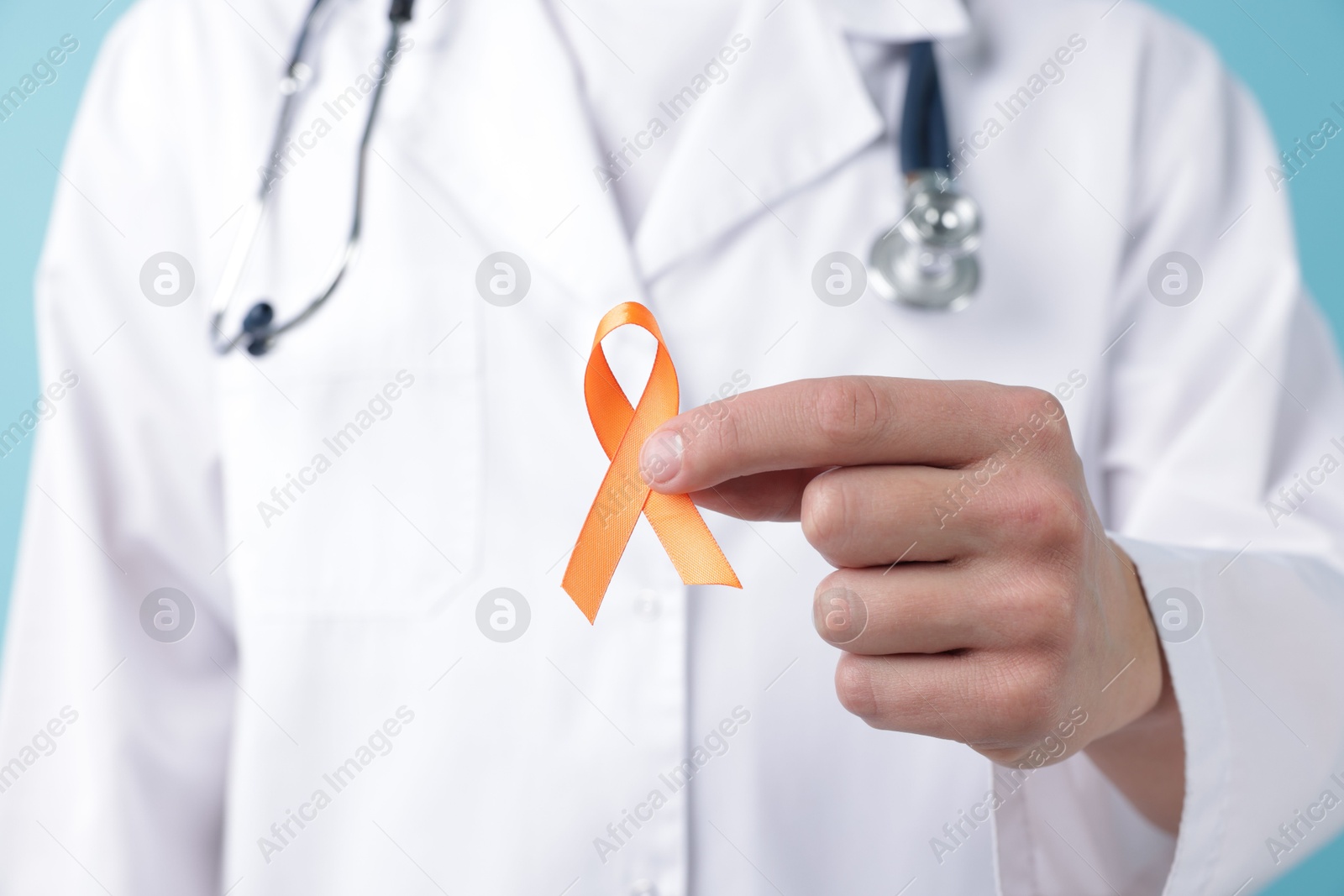 Photo of Multiple Sclerosis awareness. Doctor with orange ribbon on light blue background, closeup