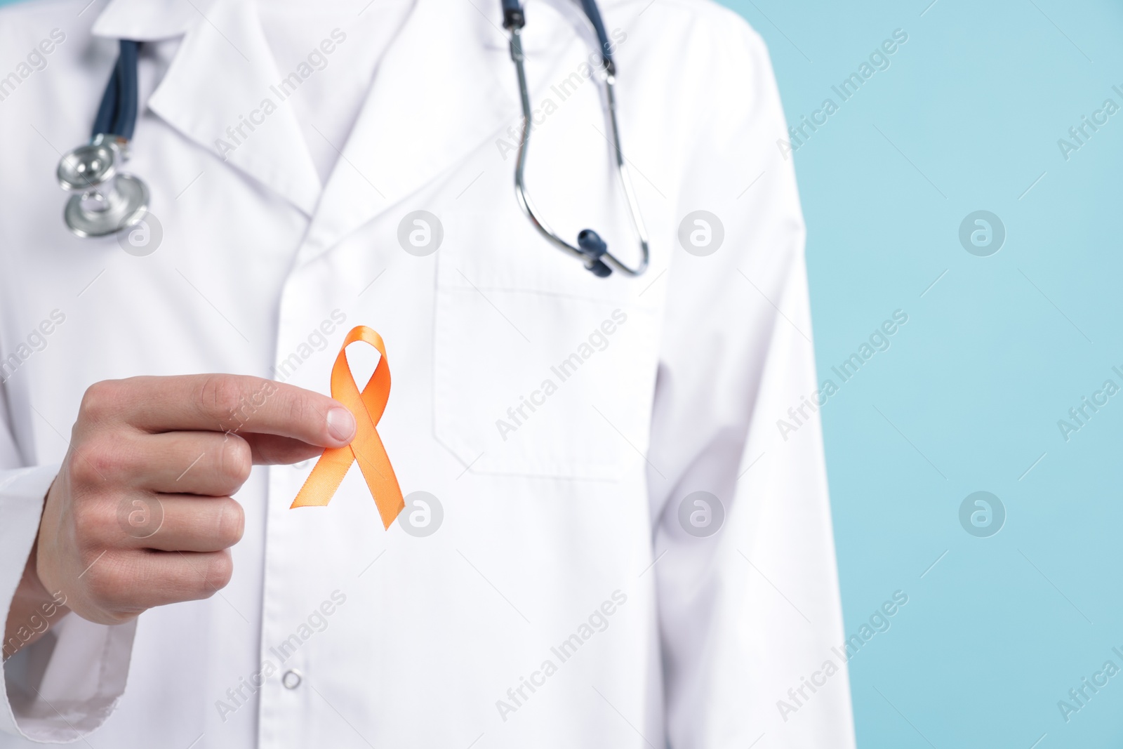 Photo of Multiple Sclerosis awareness. Doctor with orange ribbon on light blue background, closeup