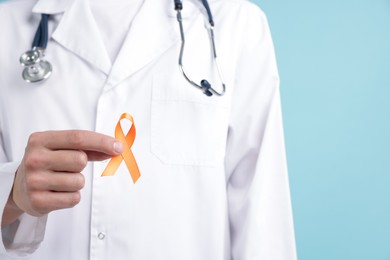 Photo of Multiple Sclerosis awareness. Doctor with orange ribbon on light blue background, closeup