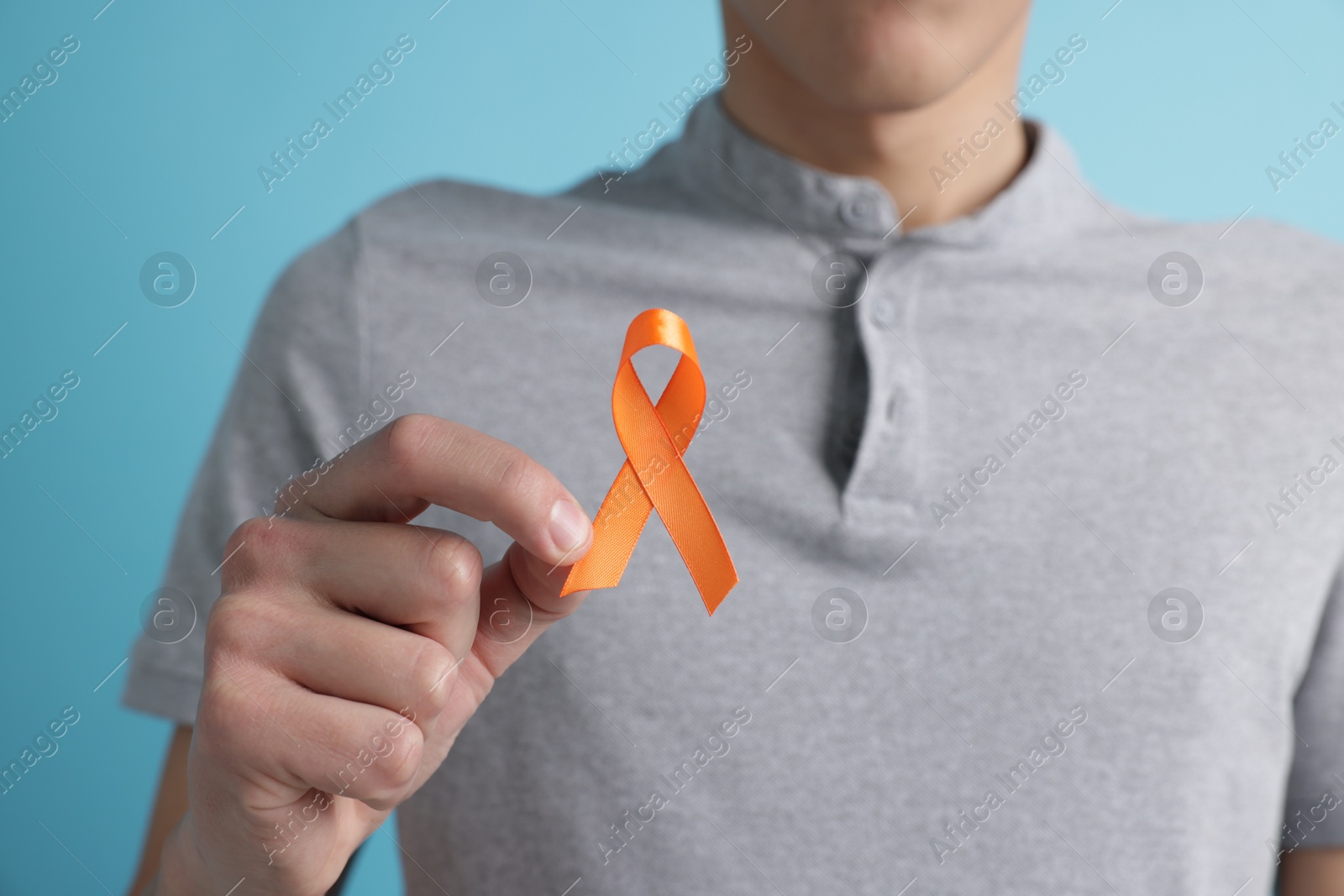 Photo of Multiple Sclerosis awareness. Man with orange ribbon on light blue background, closeup