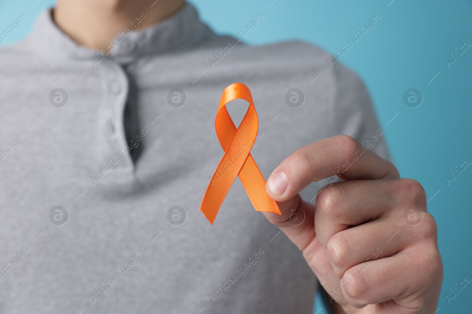 Photo of Multiple Sclerosis awareness. Man with orange ribbon on light blue background, closeup