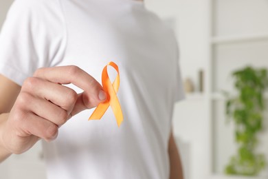 Photo of Multiple Sclerosis awareness. Man with orange ribbon indoors, closeup