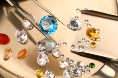 Photo of Tweezers with beautiful gemstones on light table, selective focus