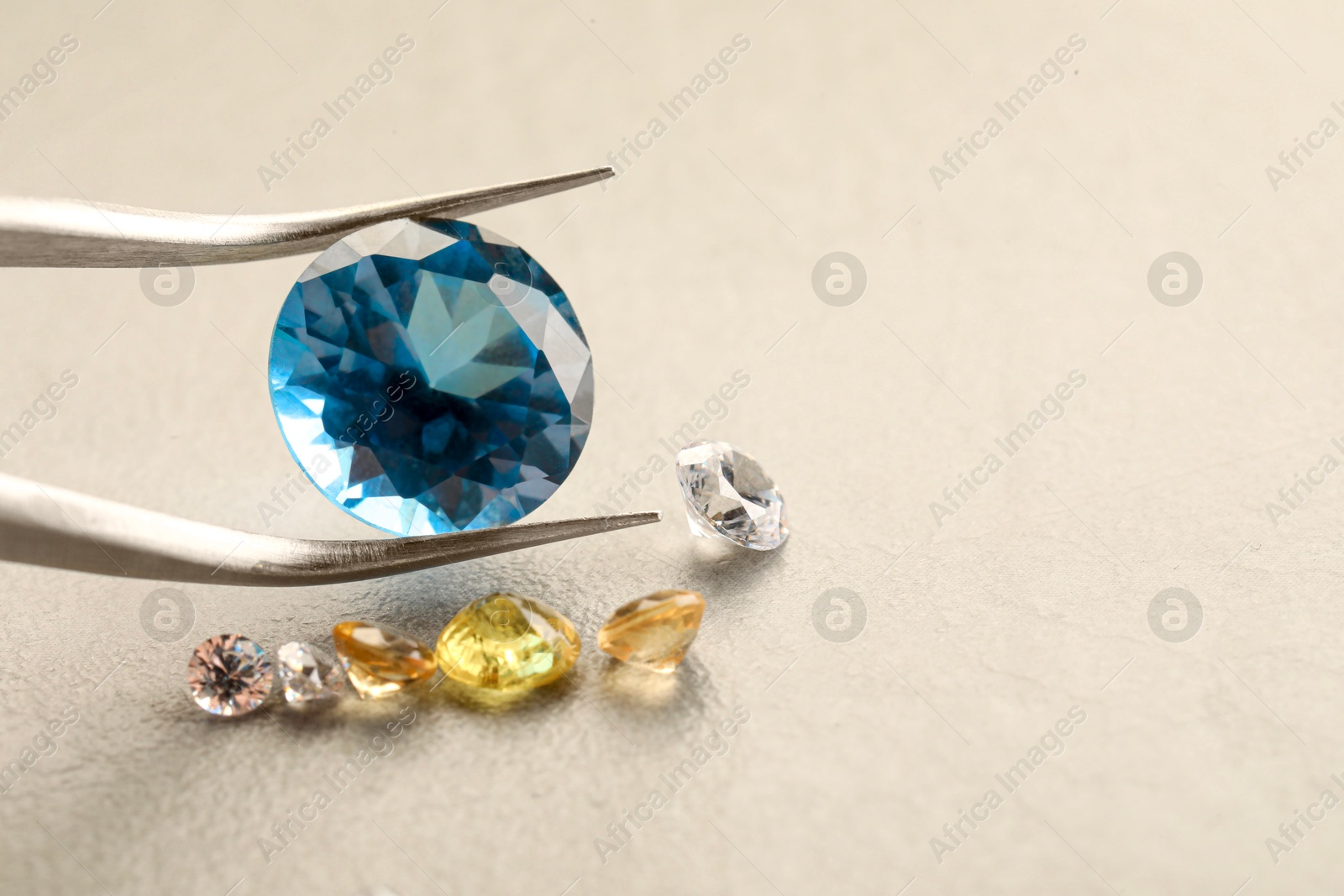 Photo of Tweezers with beautiful gemstones on light textured table, closeup. Space for text