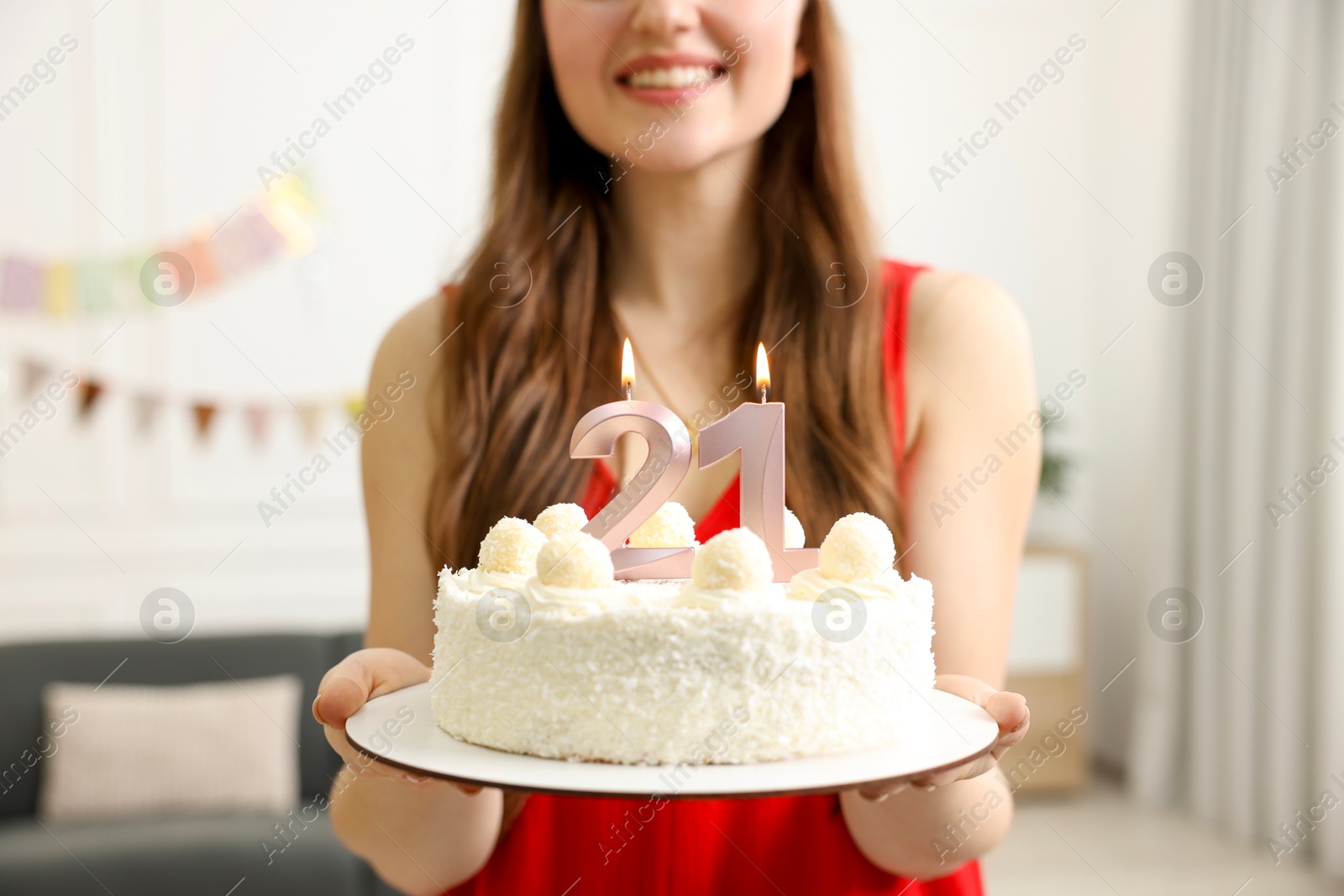 Photo of Coming of age party - 21st birthday. Happy young woman holding tasty cake with number shaped candles at home, closeup