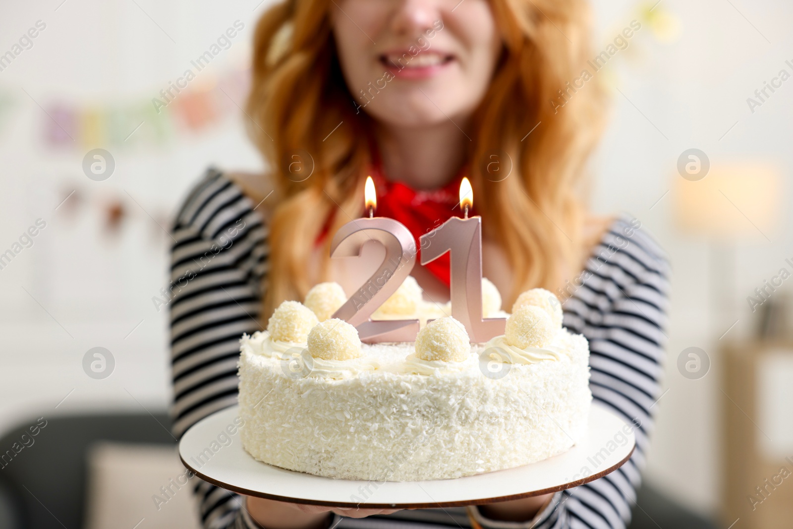 Photo of Coming of age party - 21st birthday. Young woman holding tasty cake with number shaped candles at home, closeup