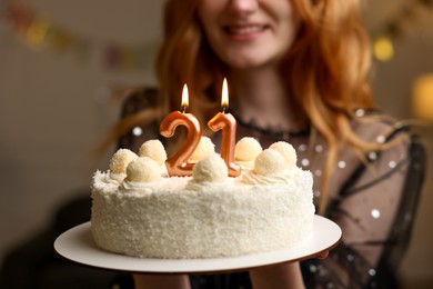 Photo of Coming of age party - 21st birthday. Happy young woman holding tasty cake with number shaped candles at home, closeup