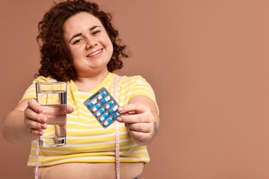 Photo of Happy plus size woman giving blister of weight loss supplements and glass of water on beige background, selective focus. Space for text