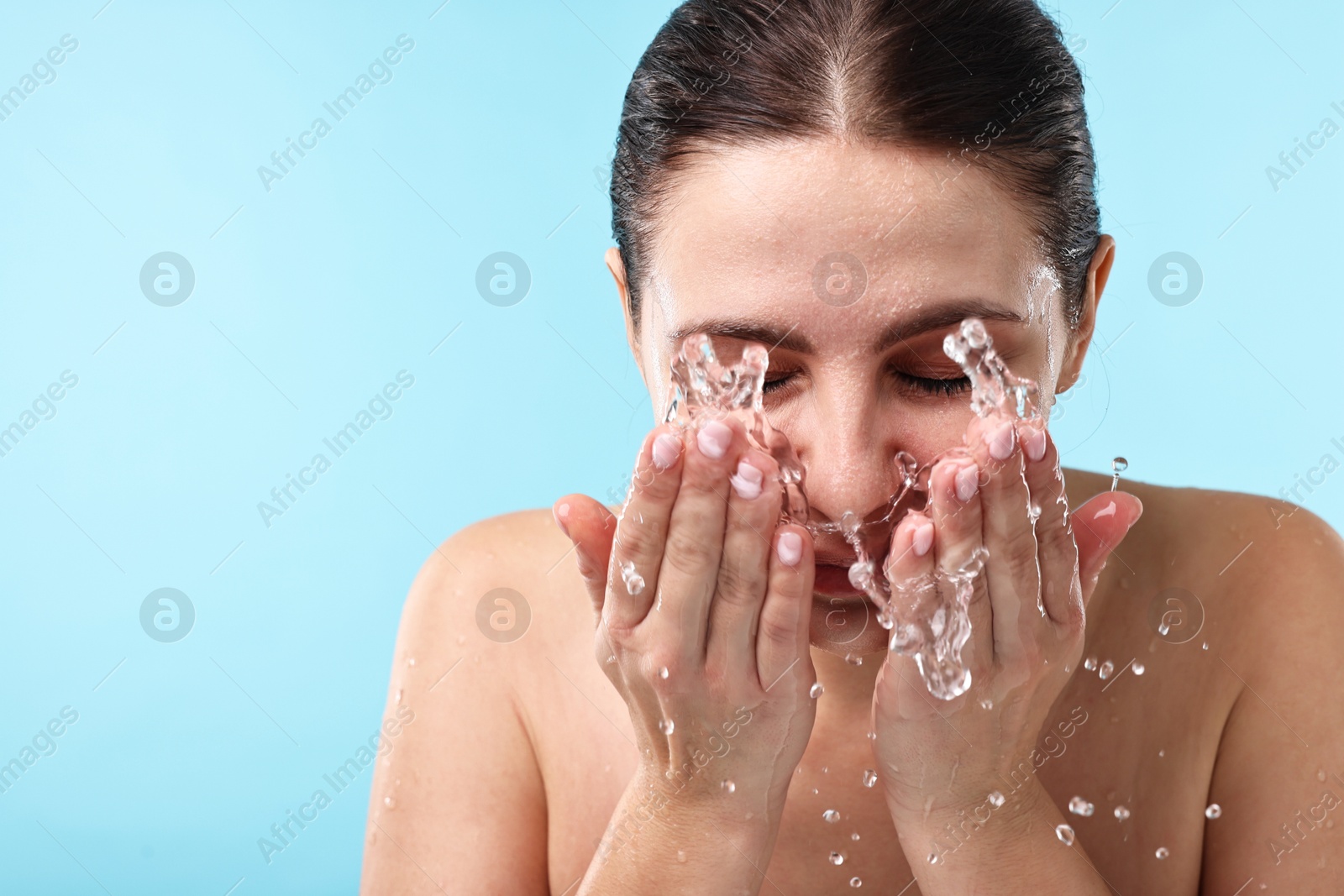 Photo of Woman washing her face on light blue background. Space for text