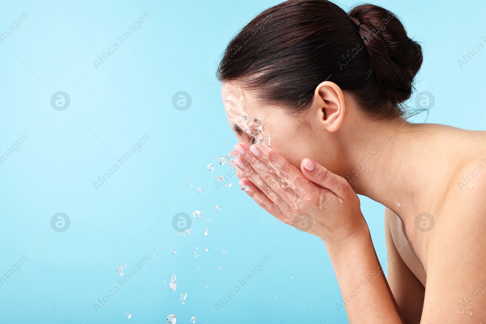 Photo of Woman washing her face on light blue background. Space for text