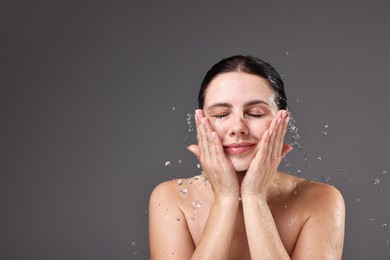 Photo of Attractive woman washing her face on grey background, space for text