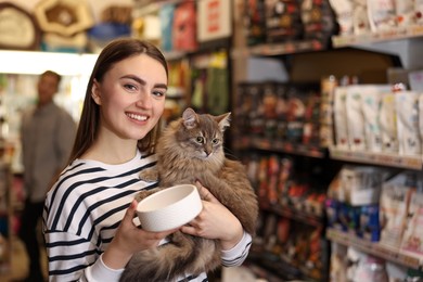 Photo of Woman with her cute cat and feeding bowl in pet shop. Space for text