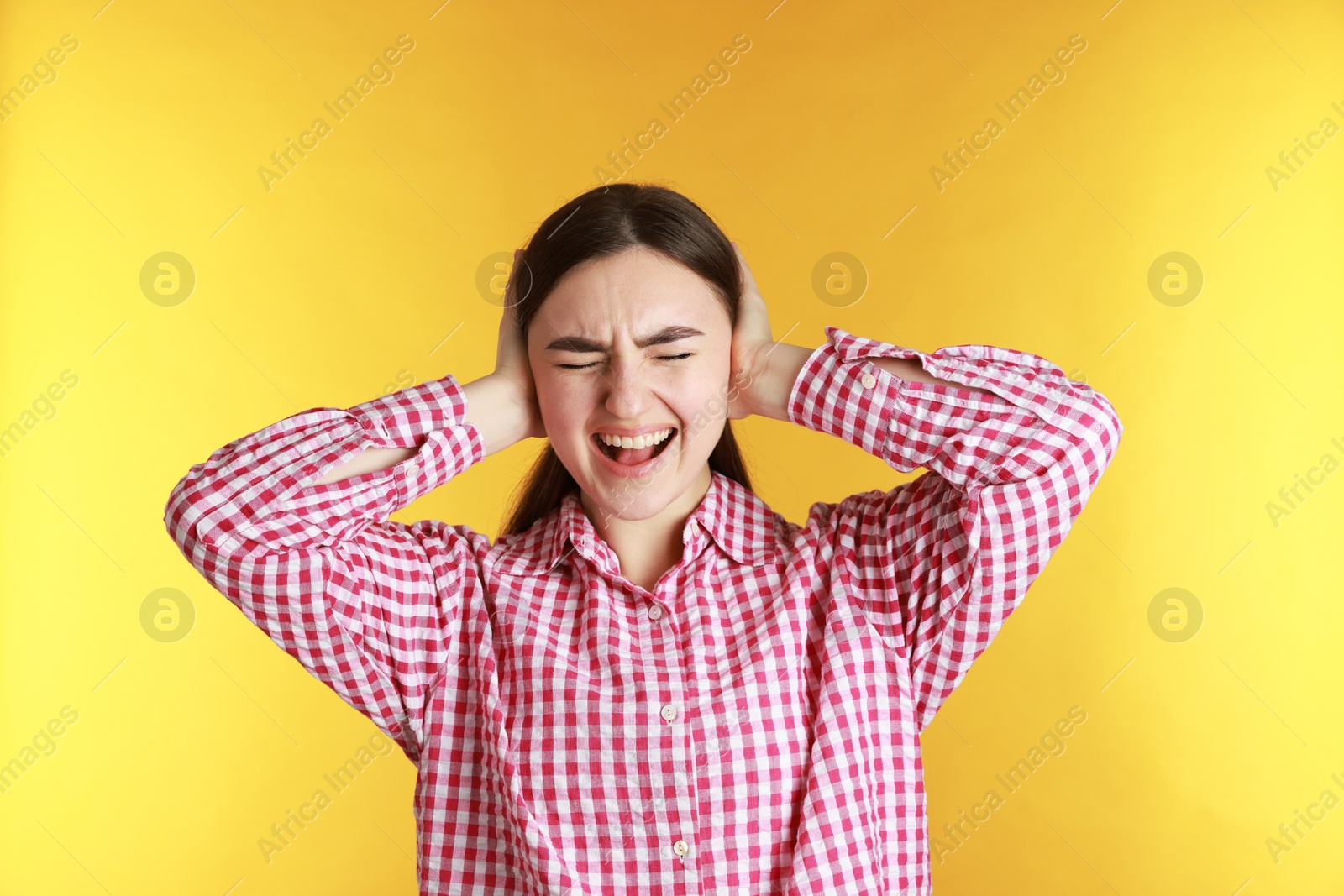 Photo of Distressed woman covering her ears from loud noise on yellow background