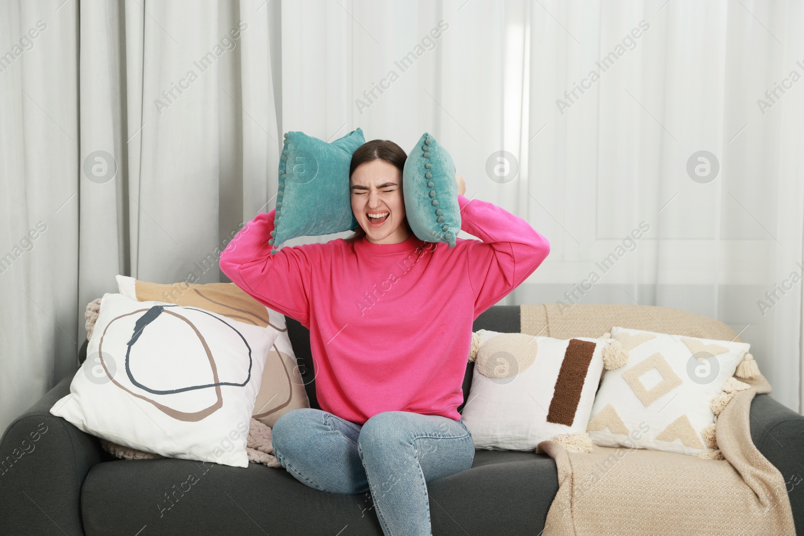 Photo of Frustrated woman covering her ears with pillows from loud noise at home