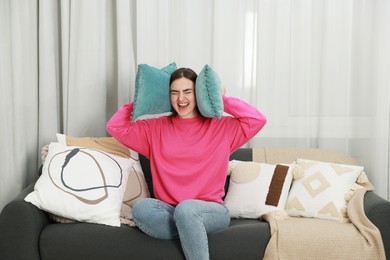 Photo of Frustrated woman covering her ears with pillows from loud noise at home