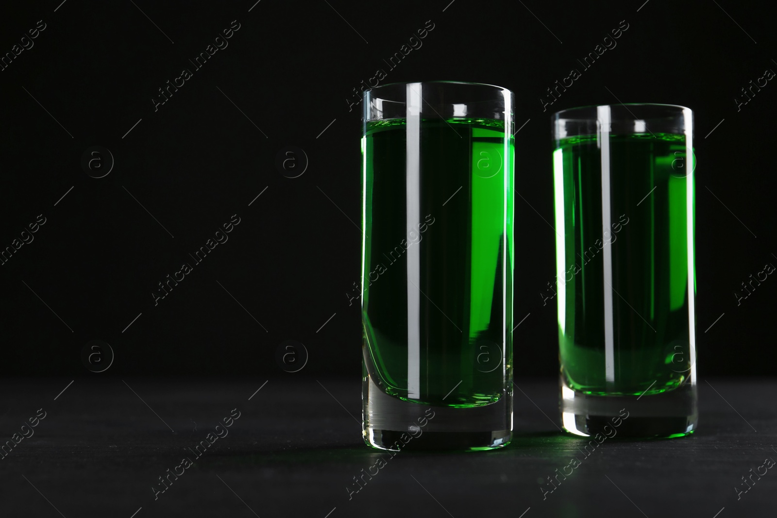 Photo of Absinthe in shot glasses on table against black background, closeup. Space for text