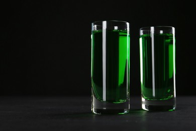 Photo of Absinthe in shot glasses on table against black background, closeup. Space for text