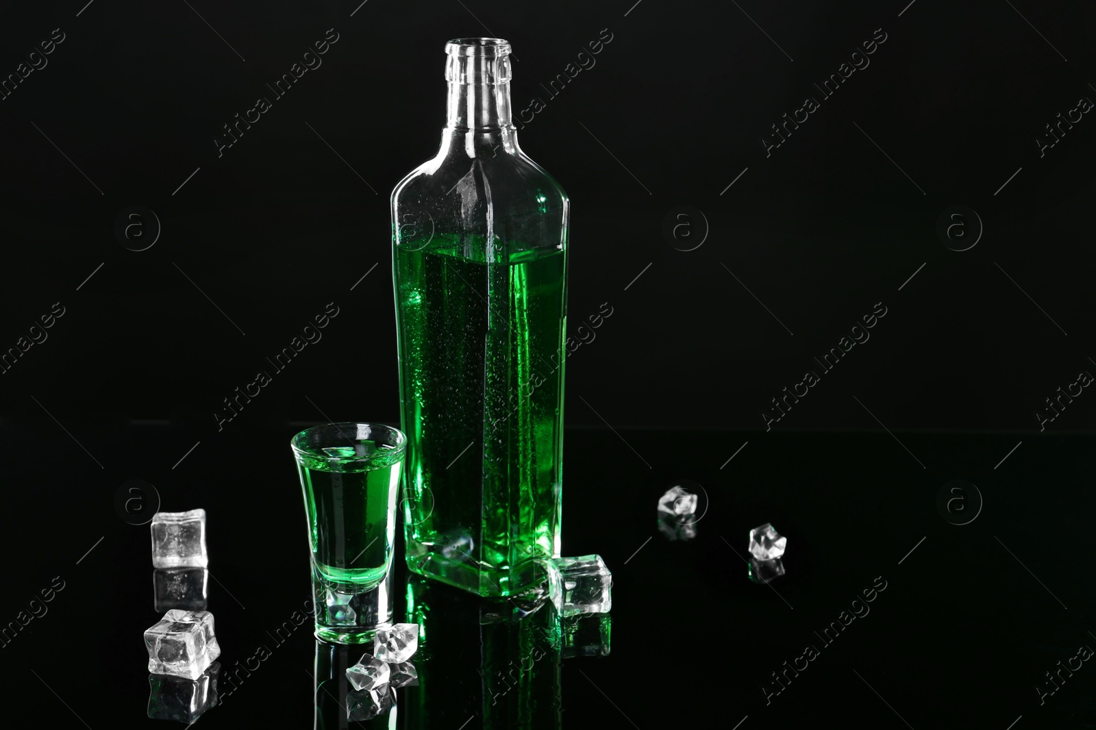 Photo of Absinthe in shot glass, bottle and ice cubes on black mirror surface, space for text