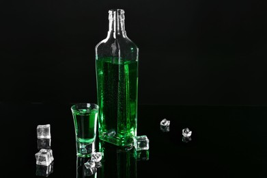 Photo of Absinthe in shot glass, bottle and ice cubes on black mirror surface, space for text