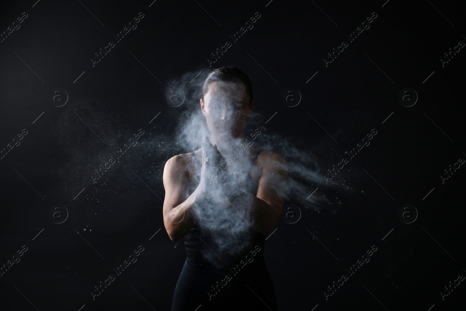 Photo of Woman clapping hands with talcum powder before training on black background